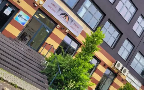 Elegancki budynek z oknami i drzwiami, z zielenią przed wejściem.