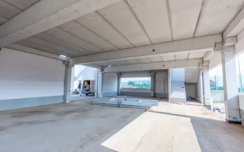 Betonowy strop teriva w stanie surowym, z widocznymi belkami i płytami. W tle samochód dostawczy i schody.