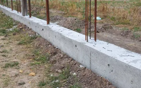 Solidna podmurówka z betonu z wystającymi prętami zbrojeniowymi, gotowa na dalsze prace budowlane.