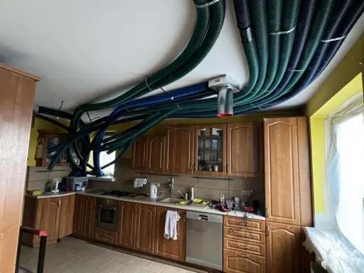 Instalacja rekuperacji w starym domu. W kuchni na suficie widać gęstą sieć zielonych i niebieskich rur wentylacyjnych.