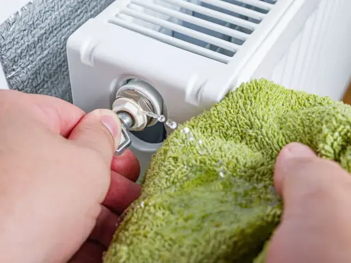Odkręcanie odpowietrznika grzejnika, gdy jest zimny na dole. Woda kapie na zieloną ściereczkę.
