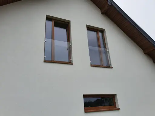 Nowoczesny portfenetr z drewnianymi ramami i szklaną balustradą na białej elewacji.