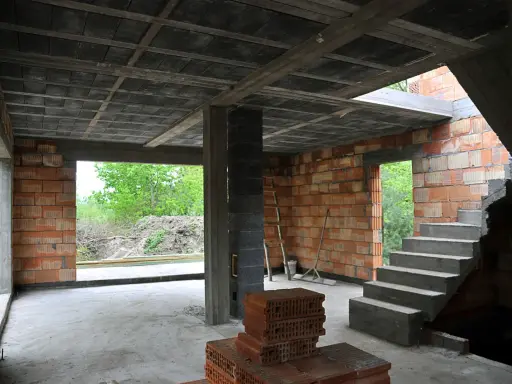 Wnętrze budowy z widocznym stropem gęstożebrowym, betonowymi schodami i ceglanymi ścianami.