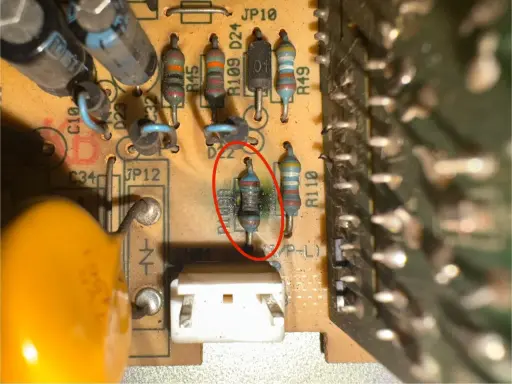 Uszkodzony opornik z czerwonym okręgiem na płytce drukowanej, obok innych elementów elektronicznych.