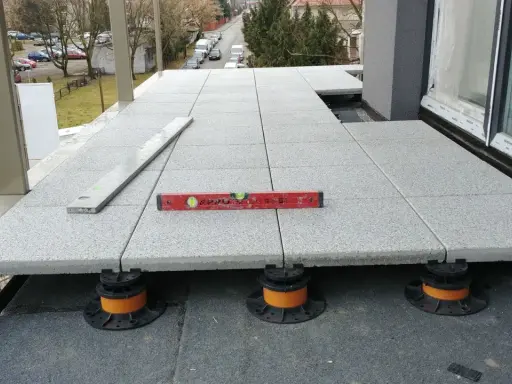Budowa tarasu wentylowanego. Płyty betonowe ułożone na regulowanych wspornikach, poziomica wskazuje idealne wypoziomowanie.