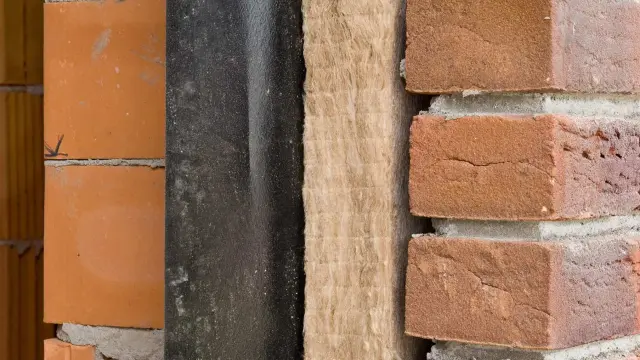 Warstwy materiałów budowlanych: cegła, czarna membrana, wełna mineralna i cegła klinkierowa. Przygotowania do ocieplenia domu.