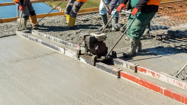 Budowlańcy używają wibrołaty do wyrównania świeżego betonu na budowie.