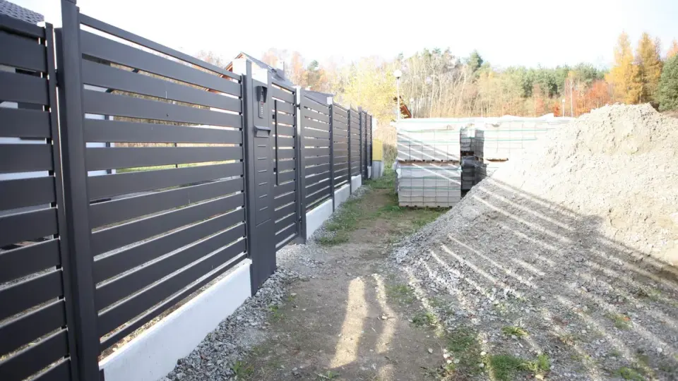 Solidny fundament pod bramę przesuwną, obok sterty kruszywa i palet z kostką brukową.